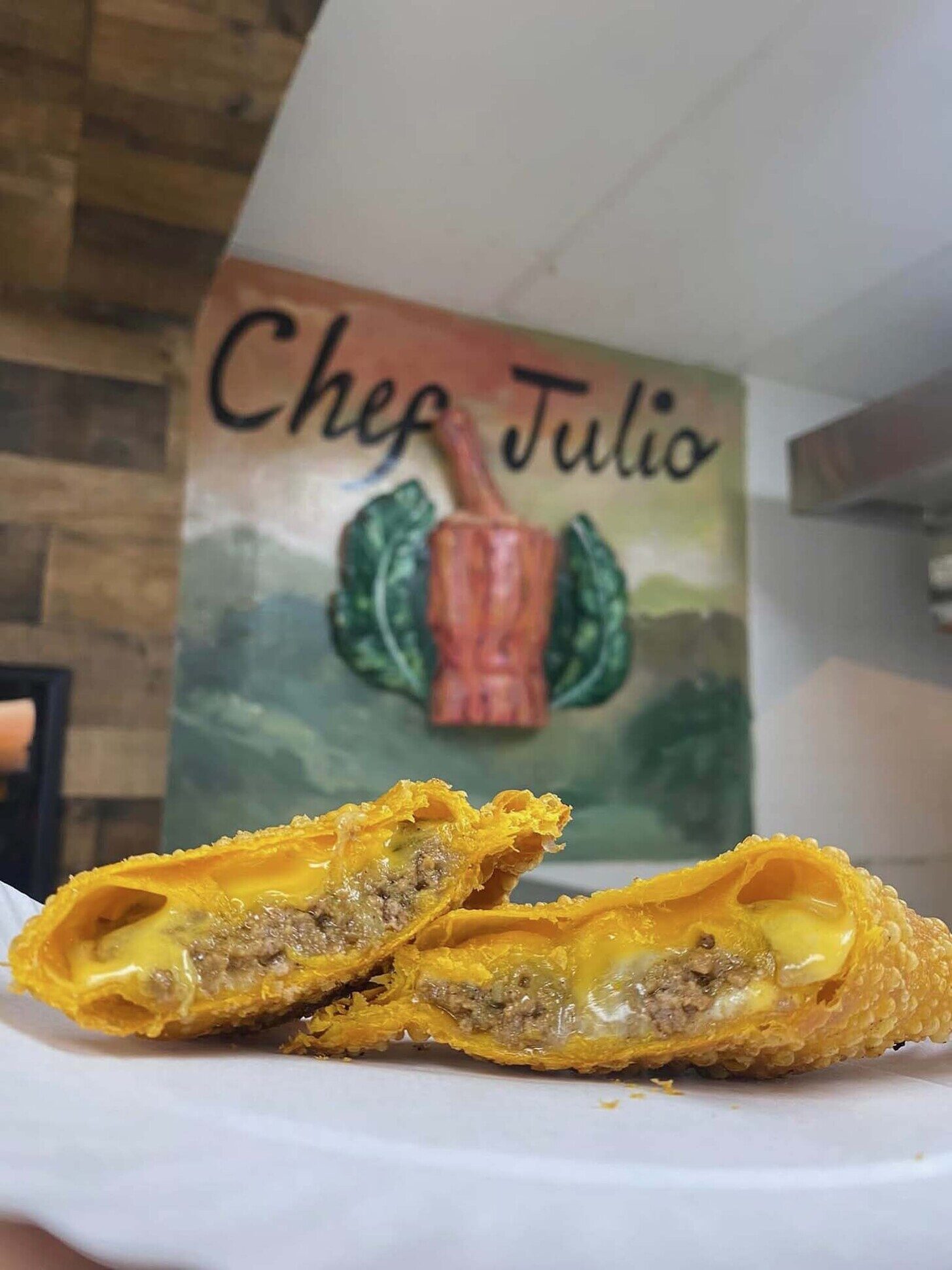 Cut-open empanada on a plate with golden crust and beef filling, Chef Julio mural in the background