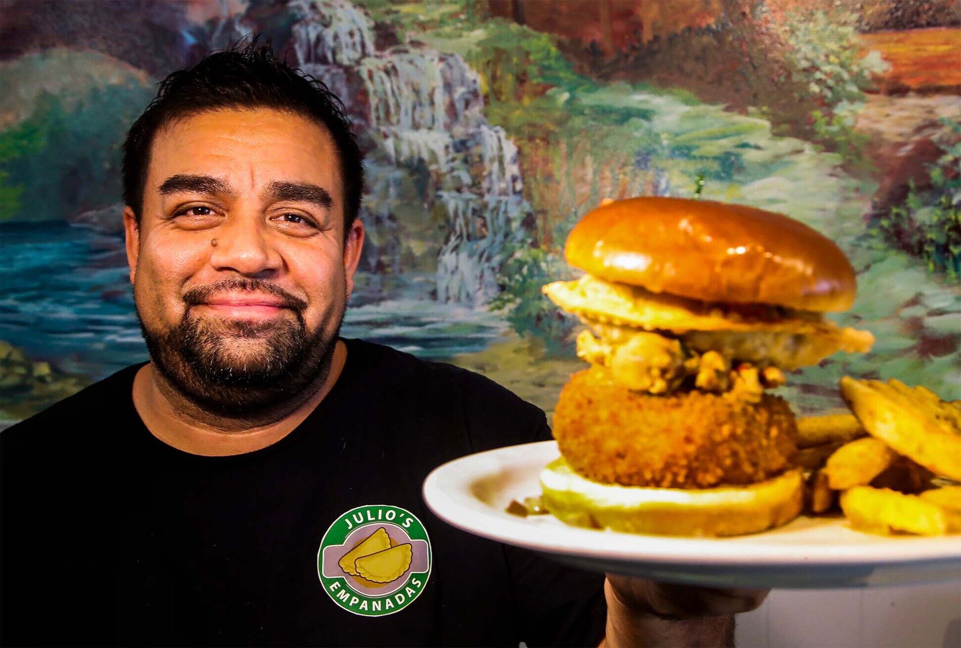 Chef Julio standing beside his Puerto Rican flag mural holding a plate
