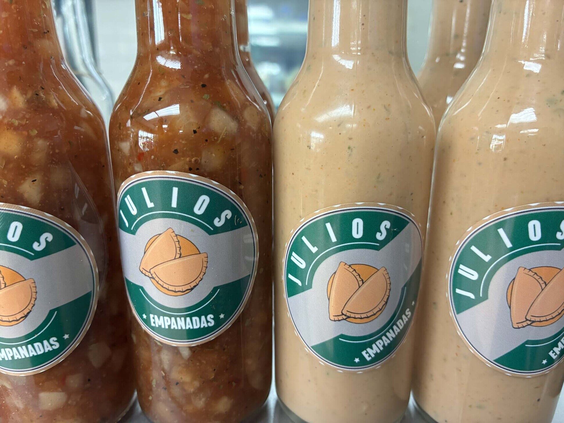 Four branded Julio's Empanadas sauce bottles - two red salsa and two cream aioli - with green and gold labels